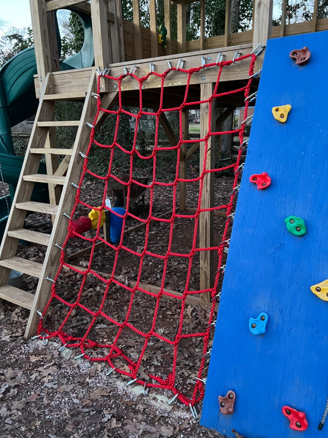 Children's playground with red net climbing structure and blue climbing wall.